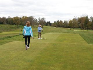 Jeremy Elwood and Alison Root on the tee ready to tee off, with Jeremy checking the time in relation to their allotted slot