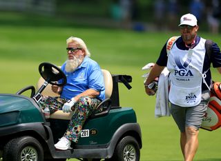 John Daly sits in a golf cart whilst his caddie walks on behind him