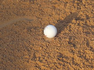 A golf ball nestled in the bunker sand