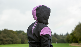 The hood of the adidas Women's Rain.RDY Golf Jacket rests on a golfers head