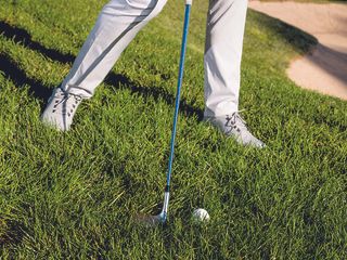 Close up of the ball sitting down in the rough grass behind the clubface