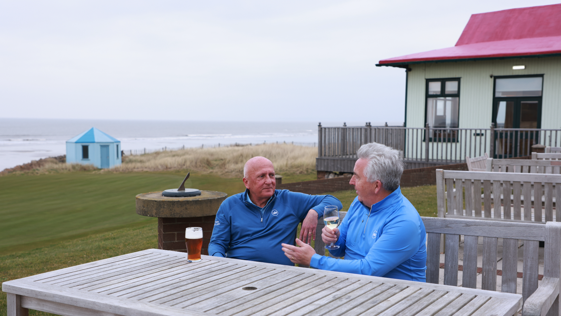 Two golfers in discussion on an outdoor table at a golf course by the sea
