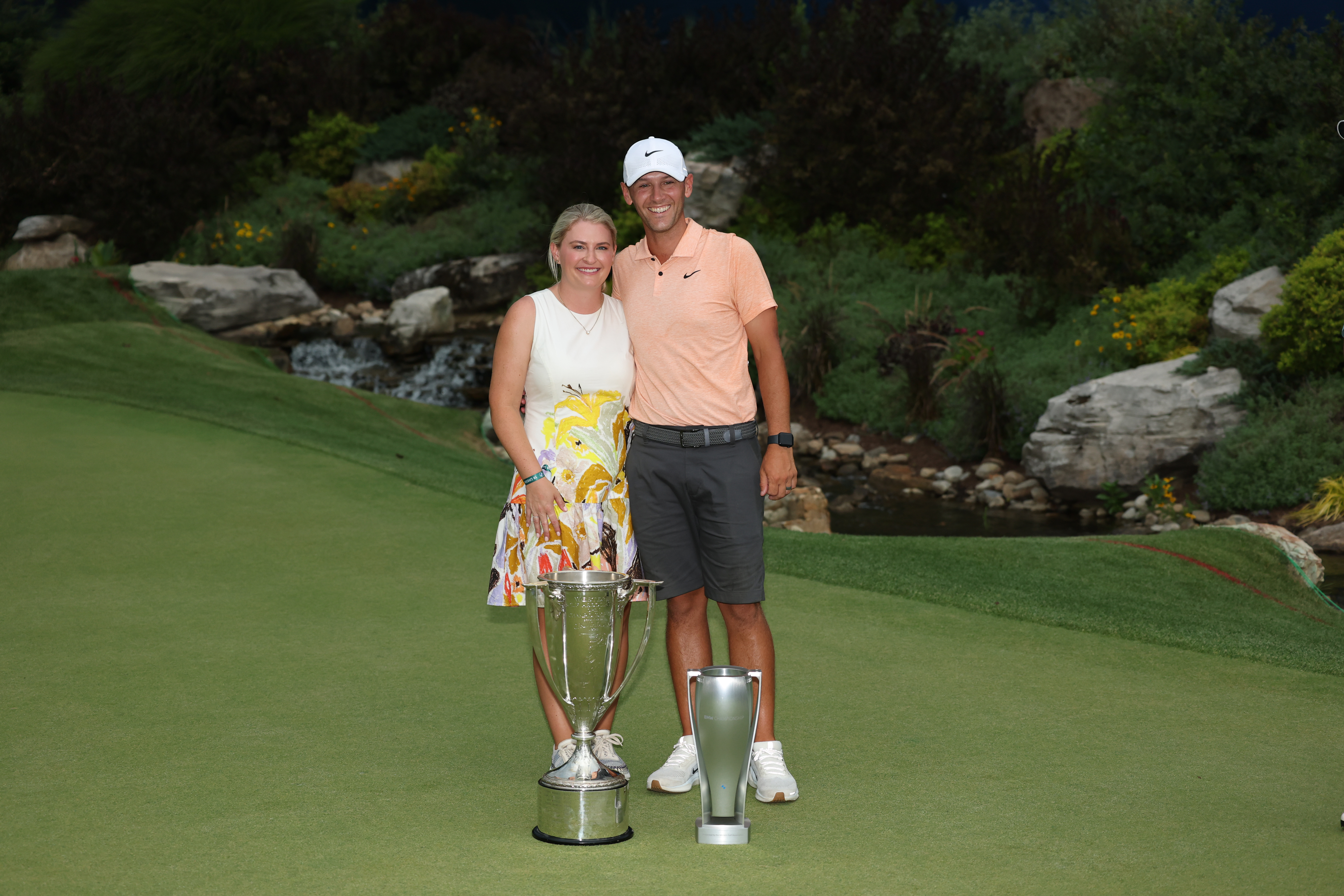 Michael Cromie (right) and his wife pose behind the BMW Championship trophies after Scottie Scheffler's win in 2025