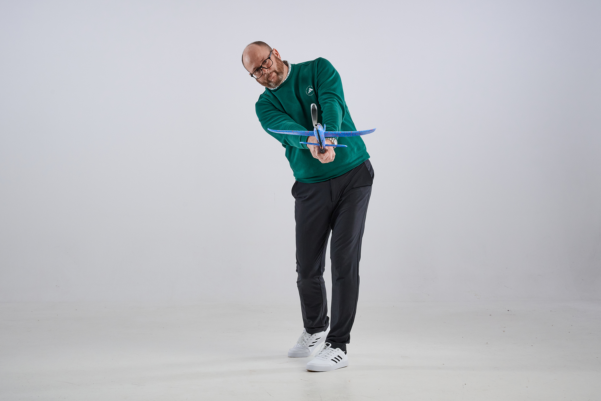 Russell Covey in the finish position of an iron shot at hip height, pointing the head of the iron down the line of the camera, with a toy plane attached to the club as part of an iron play drill